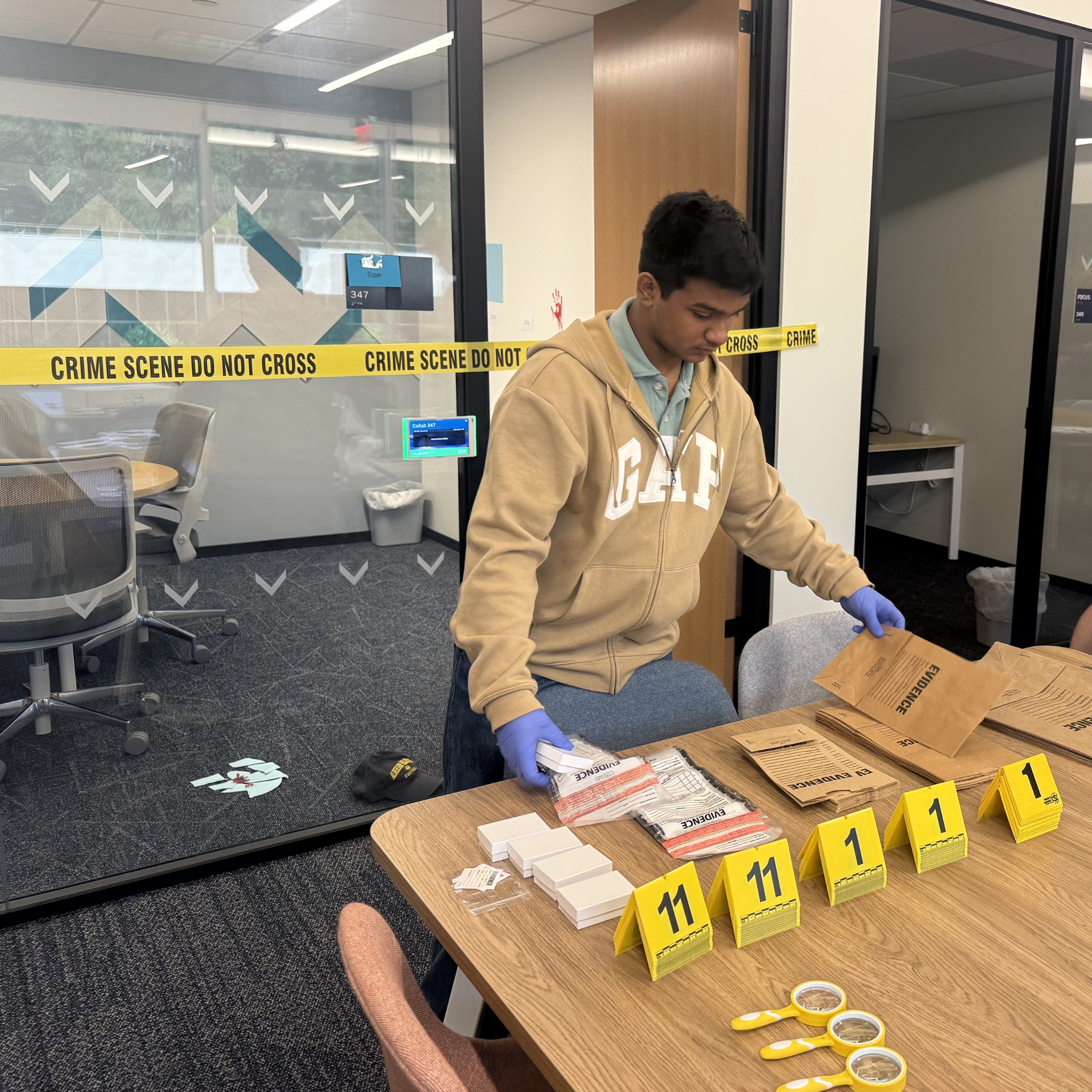 Student organizes evidence bags and numbered evidence markers outside a mock crime scene during a forensic science investigation activity.